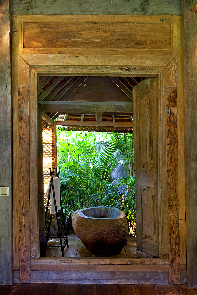 Stone bathtub set inside an open bathroom, in an old wooden house situated in the jungle. Bali, Indonesia.