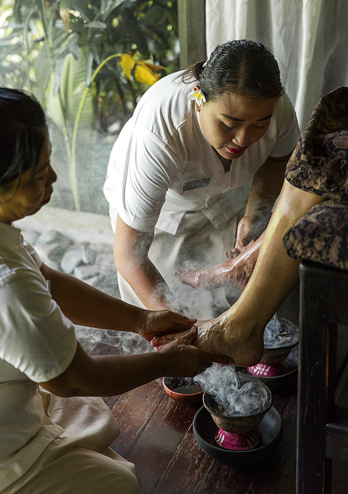 Balinese therapist performing a foot ritual with smoke from healing woodchips and incense, Bali, Indonesia.