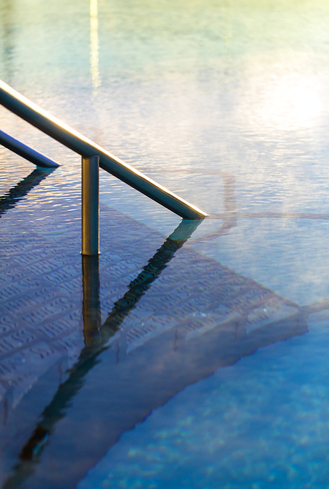 Detail shot of railing going into water in exterior pool, with morning steam. Bath, United Kingdom