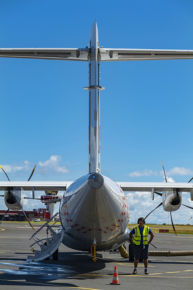 Ground worker stands at Air Tahiti ATR 72-600 aircraft on the apron of Tahiti Faa'a International Airport (PPT), Papeete, Tahiti, Windward Islands, French Polynesia, South Pacific