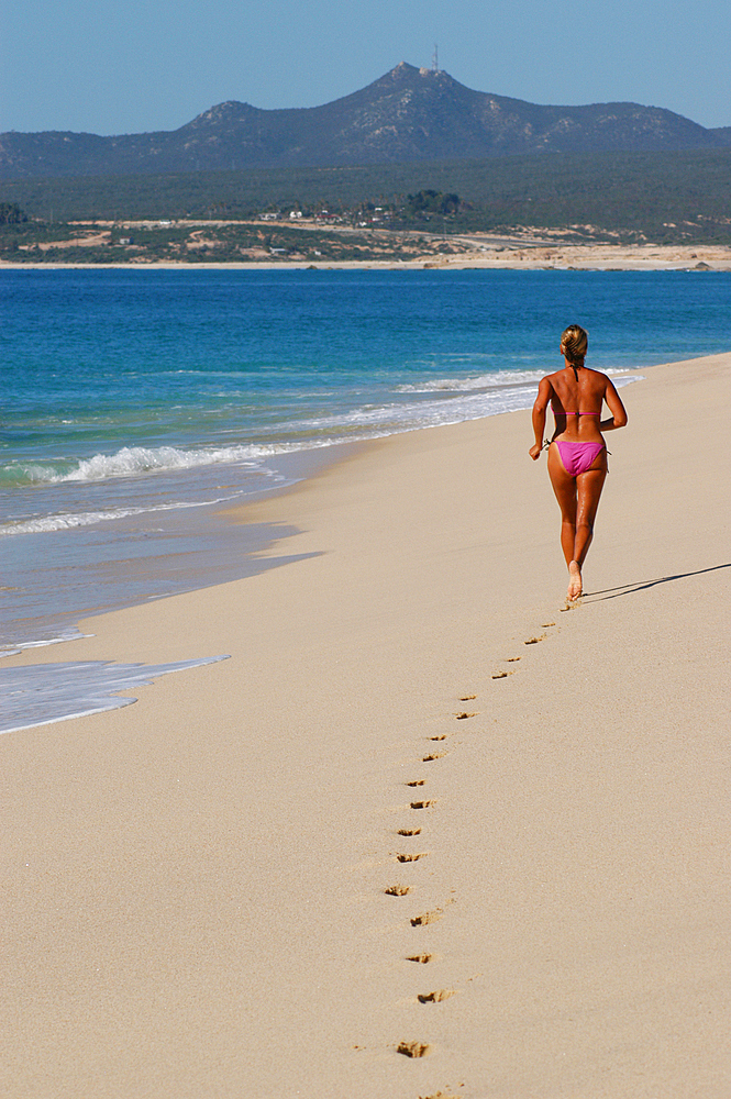 A woman in a bikini jogging along the beach of the Sea of Cortez in Cabo San Lucas, Mexico.