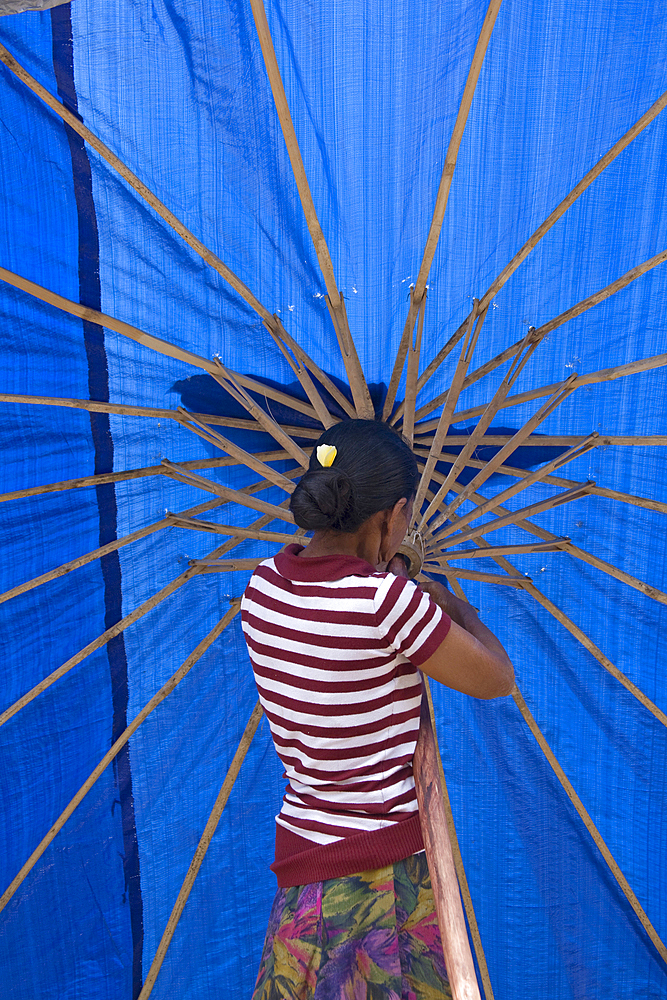 A balines woman in a striped blouse, opening a bright, blue umbrella in the market. Singaraja, Bali.