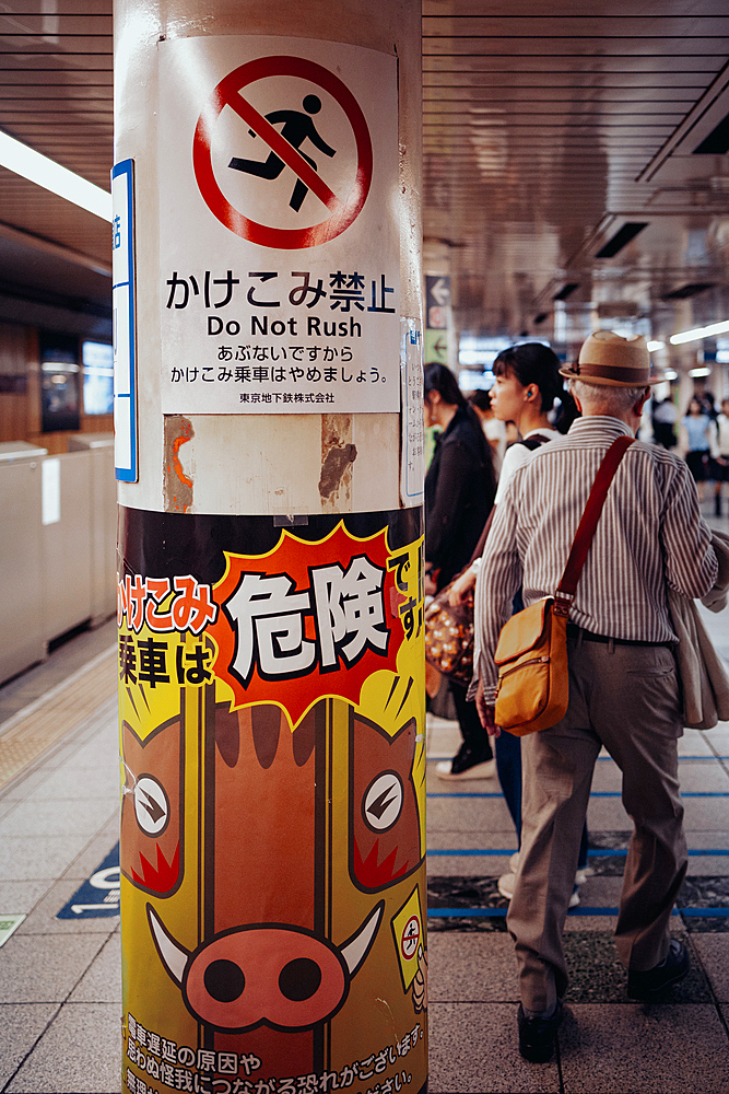 Pensioners on the subway with warning notices in the foreground, Toyko, Japan