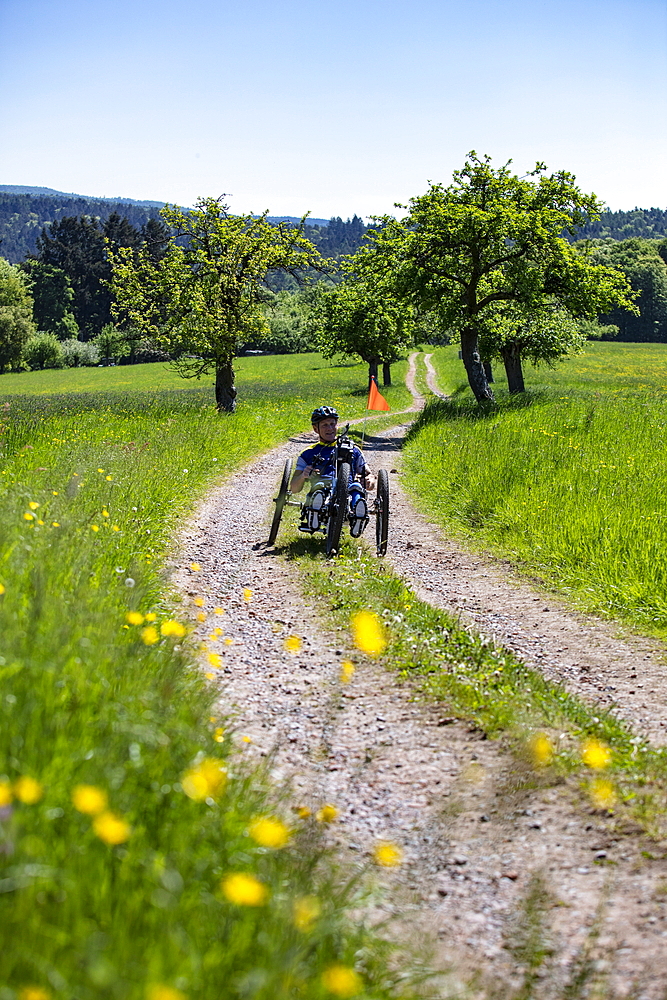 Man rides a bicycle for paraplegics on a dirt road through lush spring meadow, Heimbuchenthal, Räuberland, Spessart-Mainland, Franconia, Bavaria, Germany, Europe