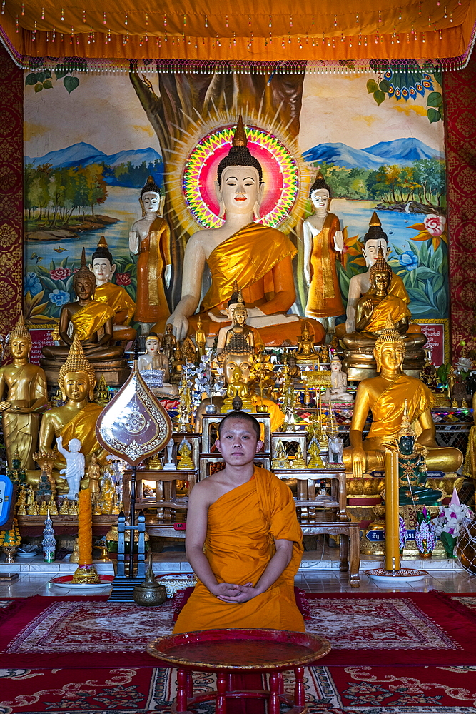 Young monk poses in front of Buddha statue at Vat Chom Khao Manilat Temple, Houayxay (Huay Xai), Bokeo Province, Laos, Asia