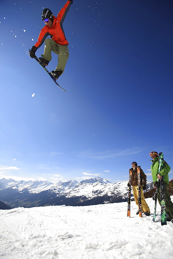 Snowboarder jumping in front of friends, See, Tyrol, Austria