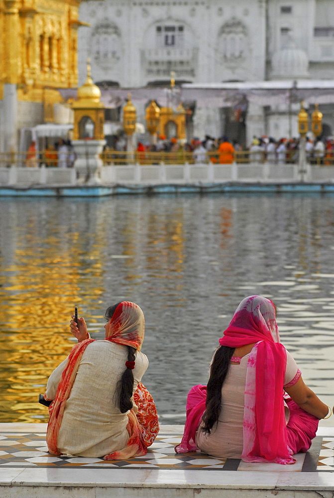 Two women in front of the Golden Temple, woman taking pictures with cell phone, Sikh holy place, Amritsar, Punjab, India, Asia