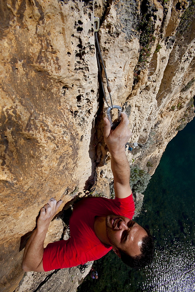 A young man climbing above the Inland Sea, he places natural protection, Dwerja Bay, Gozo, Malta, Europe