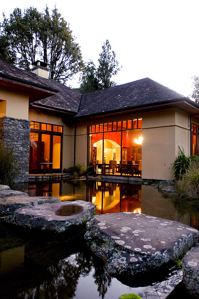 View over a pond at the illuminated windows at the Treetops Lodge in the evening, North Island, New Zealand, Oceania