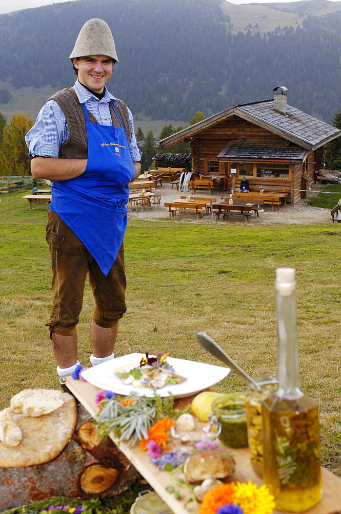 Laughing man and cookout in front of an alpine hut, Alpe di Siusi, South Tyrol, Italy, Europe