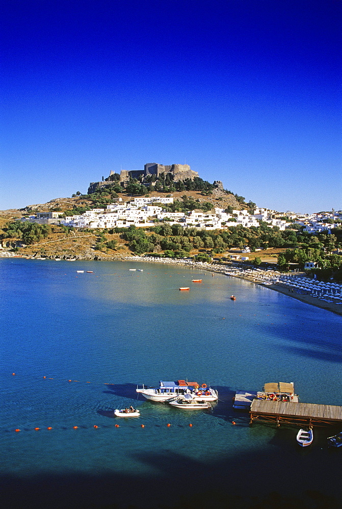 View at bay with beach, city and acropolis under blue sky, Lindos, Island of Rhodes, Greece, Europe