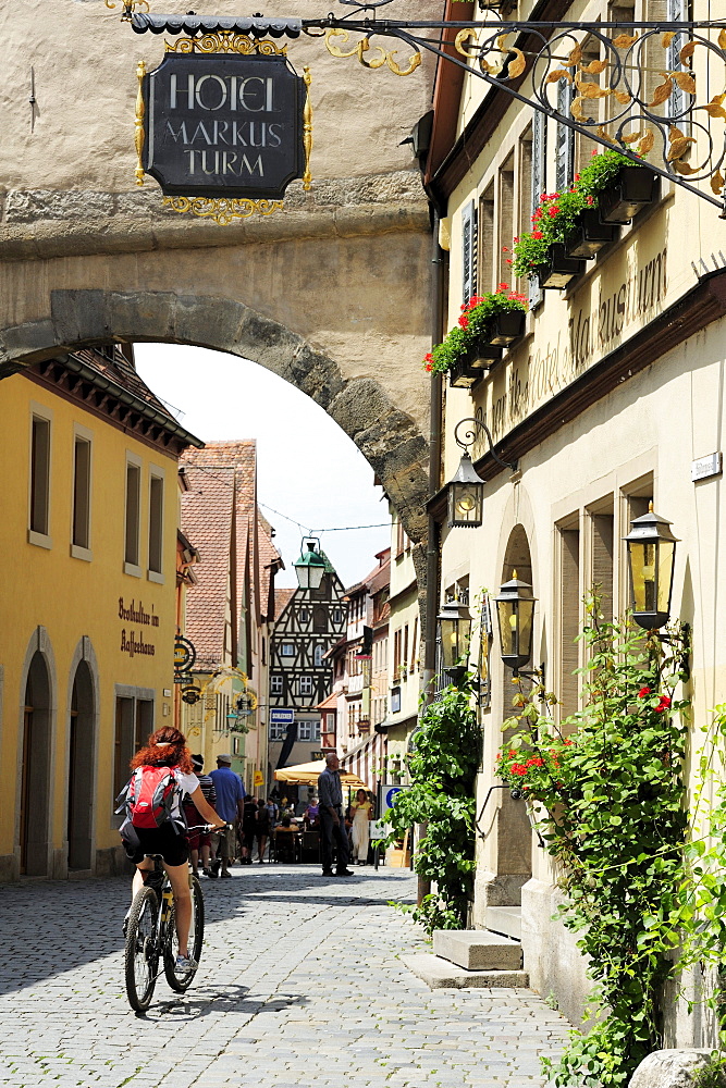 Female cyclist passing cobblestone, Roederbogen, Rothenburg ob der Tauber, Altmuehltal cycle trail, Bavaria, Germany