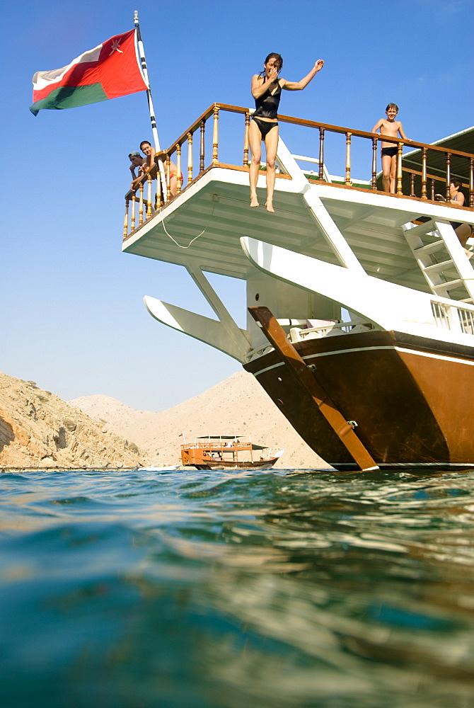 Woman jumping from a boat into the sea, Boat with tourists, Dhow, Haijar Mountains, Musandam, Oman