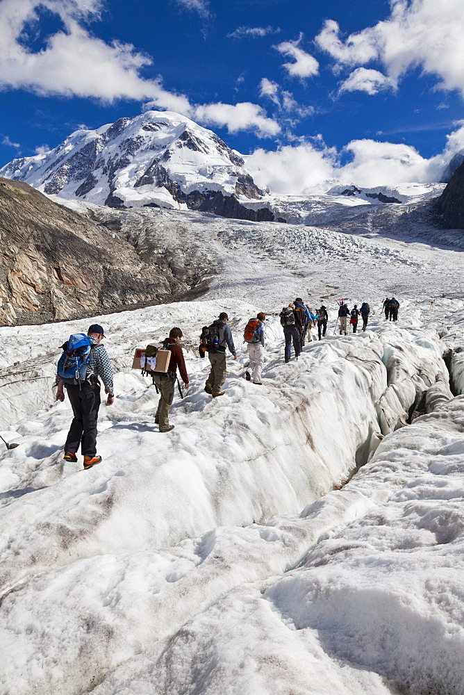 People hiking on grenz glacier to Monte Rosa hut, Liskamm in background, Zermatt, Canton of Valais, Switzerland, myclimate audio trail