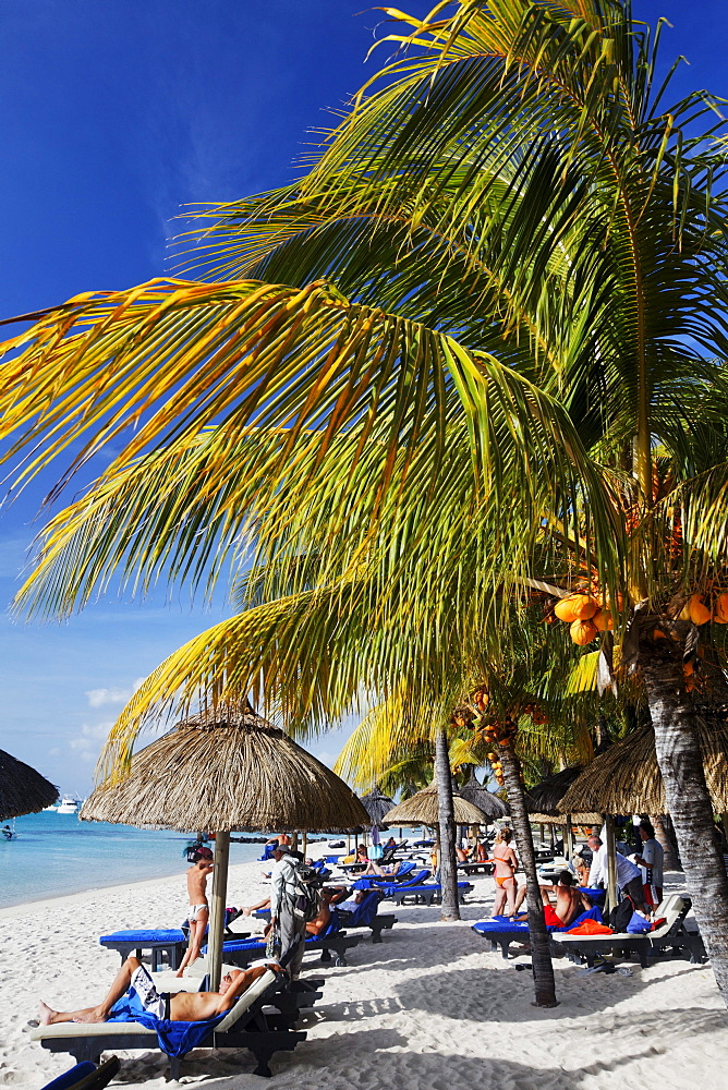 Palm trees and people on the beach of Beachcomber Hotel Paradis &amp; Golf Club, Mauritius, Africa