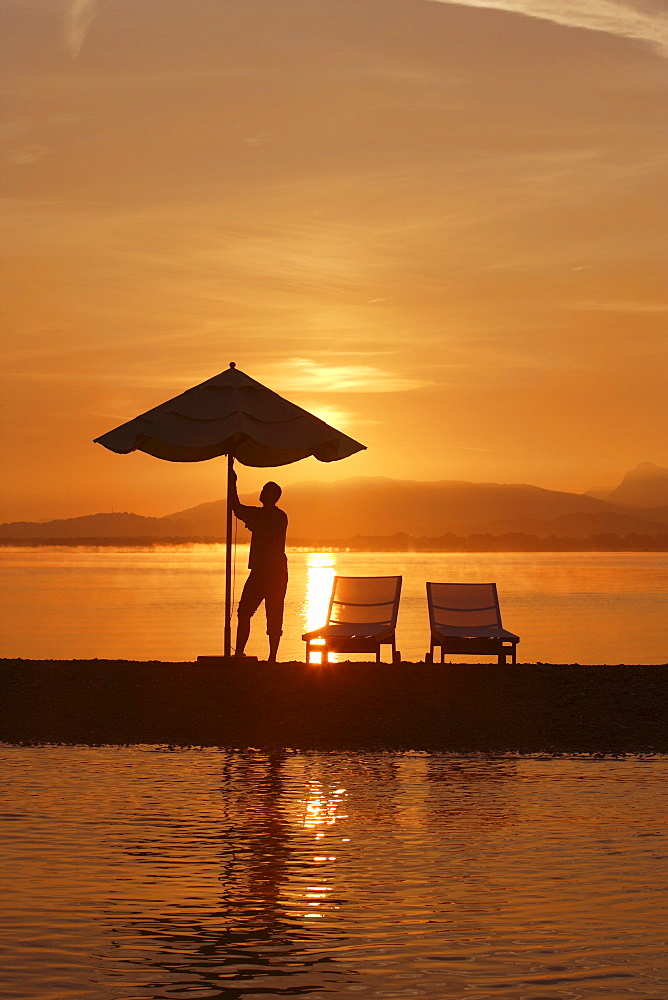 Sunrise at Krautinsel, man opening sunshade, Lake Chiemsee, Chiemgau, Bavaria, Germany