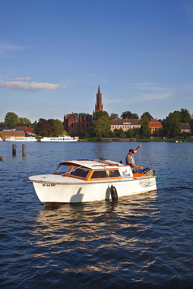 Fisherman in motorboat, view over Fleesensee lake to Malchow monastery, Mueritz-Elde-canal, Mecklenburg lake district, Mecklenburg Western-Pomerania, Germany, Europe