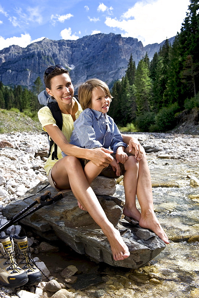 A woman and a boy sitting on a rock at the riverbank, South Tyrol, Italy, Europe