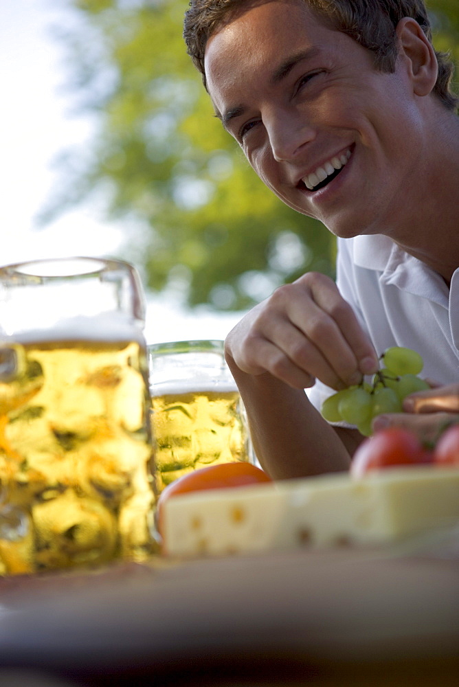 Young man with snack and beer stein in beergarden near Lake Starnberg, Bavaria, Germany