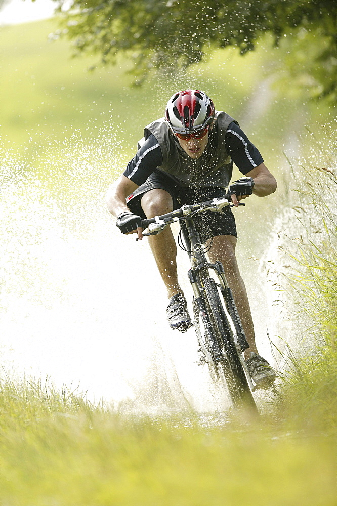 Mountainbiker riding through a puddle of water, Garmisch-Partenkirchen, Upper Bavaria, Bavaria, Germany