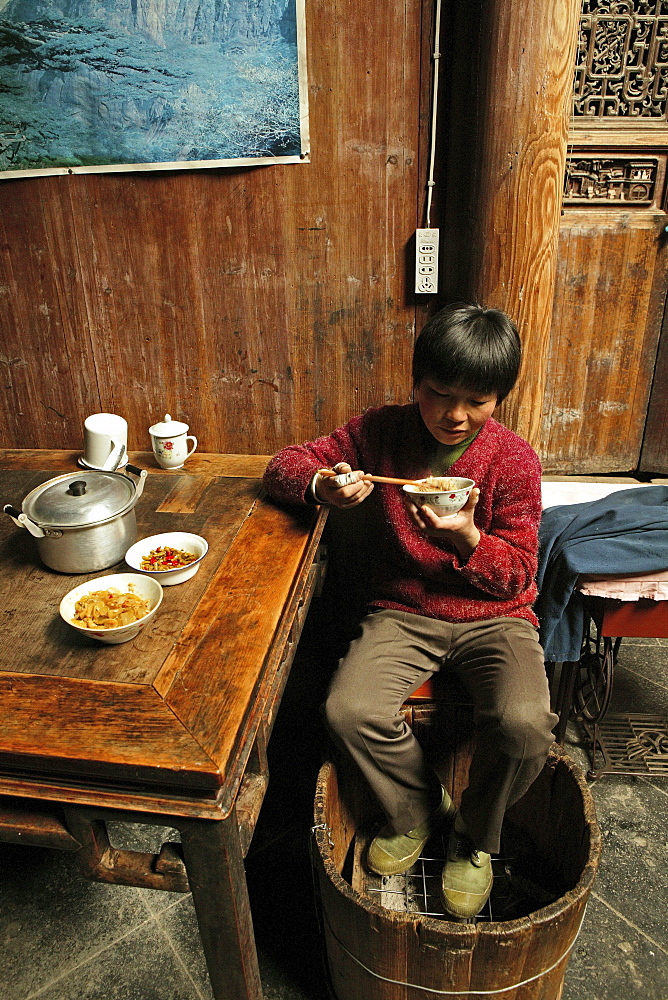 A boy eating and warming his feet at a foot warmer, Hongcun, Huang Shan, China, Asia