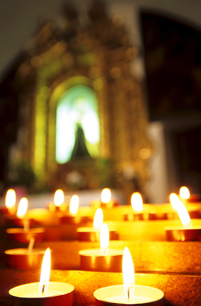 sacrifice candles and altar with picture of the Virgin Mary out of focus, Chiesa di San Stefano, Belluno, Italy