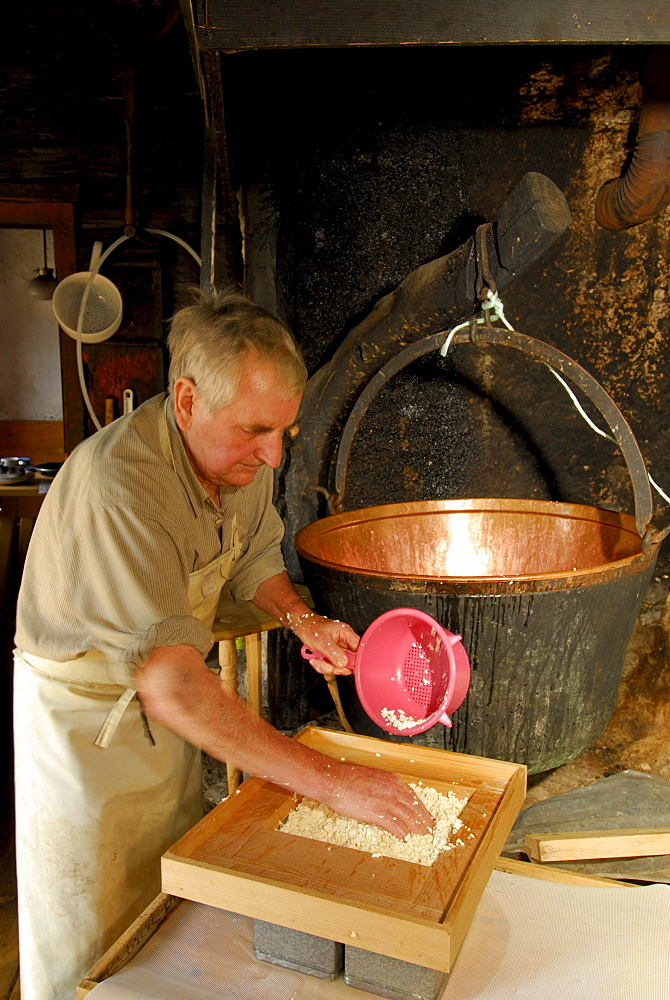 alpine cowboy making cheese in front of copper kettle, Ranggenalm, Kaiser range, Tyrol, Austria