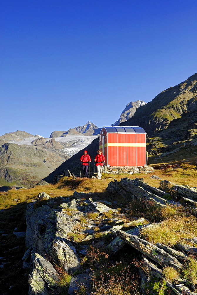 Two hikers at bivouac at Passo Canfinal (Passo Confinal), Bivacco Rasconi e Anghileri, peak Piz Roseg in background, Bernina range, Italy