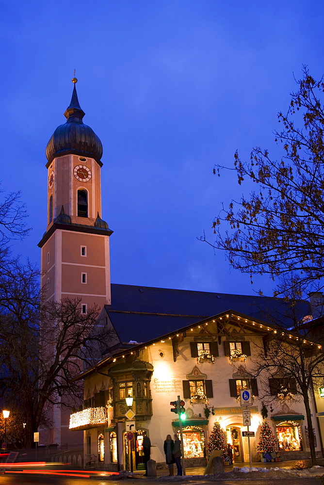 Christmassy decorated and illuminated house in the evening, church St. Martin in background, Garmisch, Garmisch-Partenkirchen, Germany