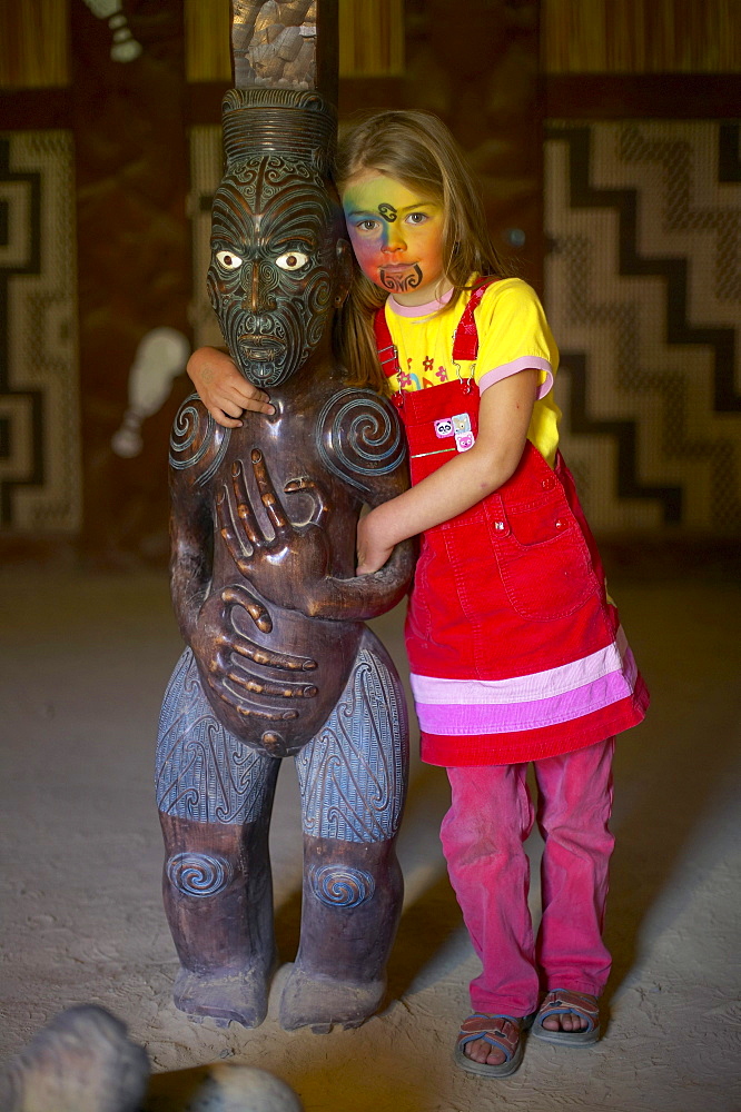 Girl with facepainting (like a Maori Moko - Tatoo), wooden Maori sculpture in Marae, celebrations on Waitangi Day, Okains Bay Museum, Bank`s Peninsula, east coast, South Island, New Zealand