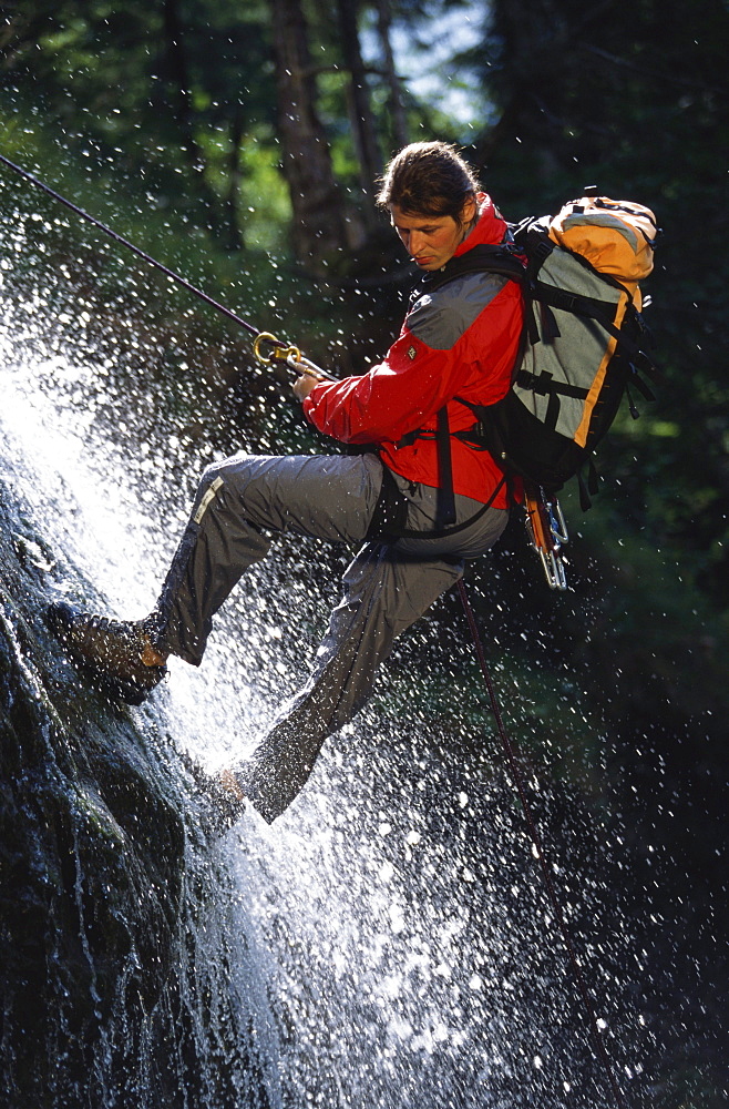 Man climbing, descending down a waterfall. Lake Sylvenstein, Upper Bavaria, Bavaria, Germany