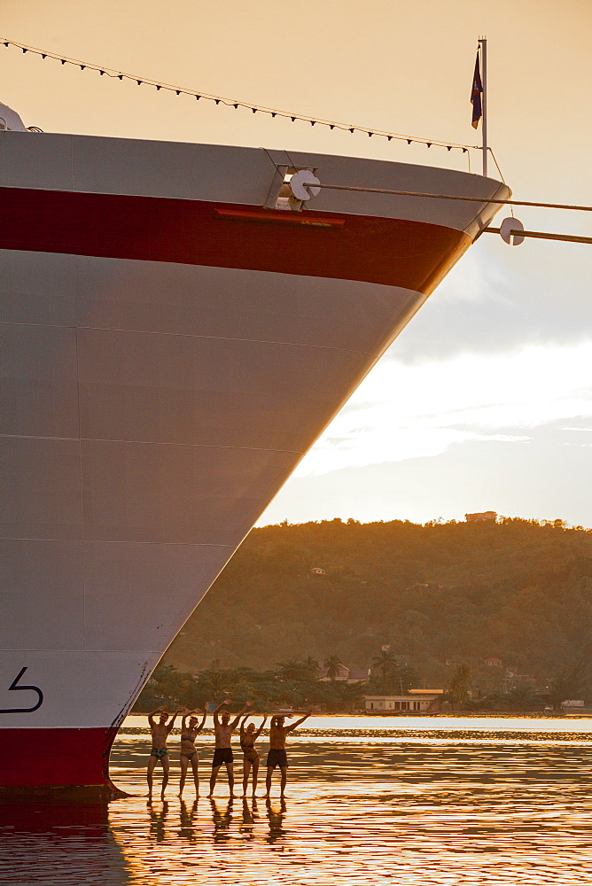 Five young people performing a sunset dance on the bulbous bow of the cruise ship MS Deutschland (Reederei Peter Deilmann), harbour of Port Antonio, Portland, Jamaica, Caribbean