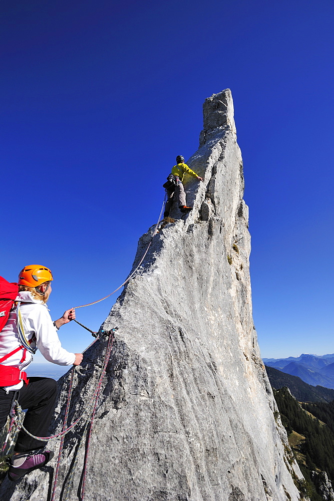 Young woman belaying climber at pinnacle, Kampenwand, Chiemgau Alps, Chiemgau, Upper Bavaria, Bavaria, Germany