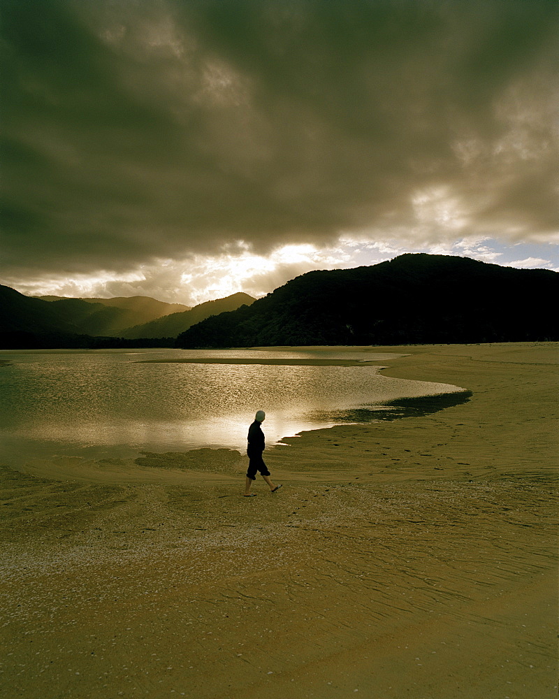 A man on shore of Awaroa Inlet at sunset, Abel Tasman National Park, North Coast, South Island, New Zealand