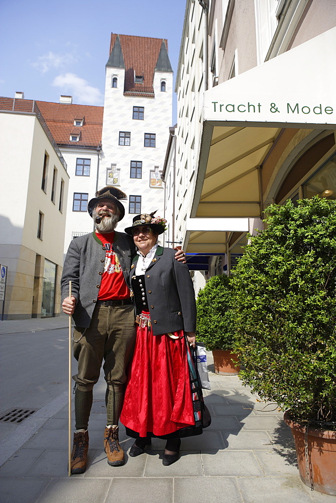 Mature couple wearing traditional costumes, tower of Alter Hof in the background, Munich, Bavaria, Germany