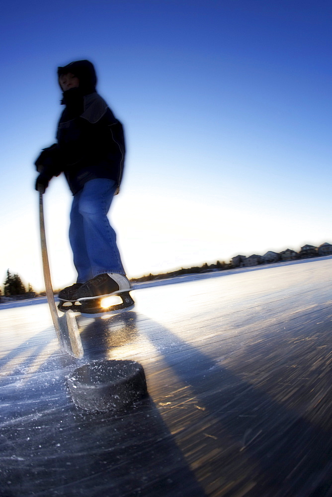 Boy Ice Skating on Lake with Hockey Stick and Puck, Calgary, Alberta