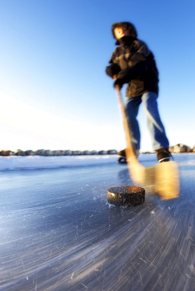 Boy Ice Skating on Lake with Hockey Stick and Puck, Calgary, Alberta