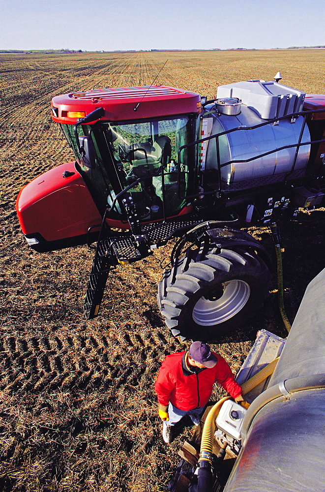 Farmer loads high Clearance Sprayer with liquid Fertilizer for application to a recently Seeded Wheat Field, near Dugald, Manitoba