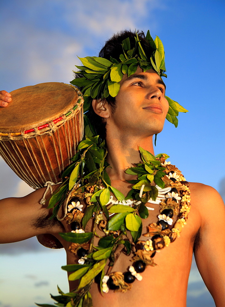 Hawaii, Oahu, Polynesian man with drum along coast, Sunrise light.