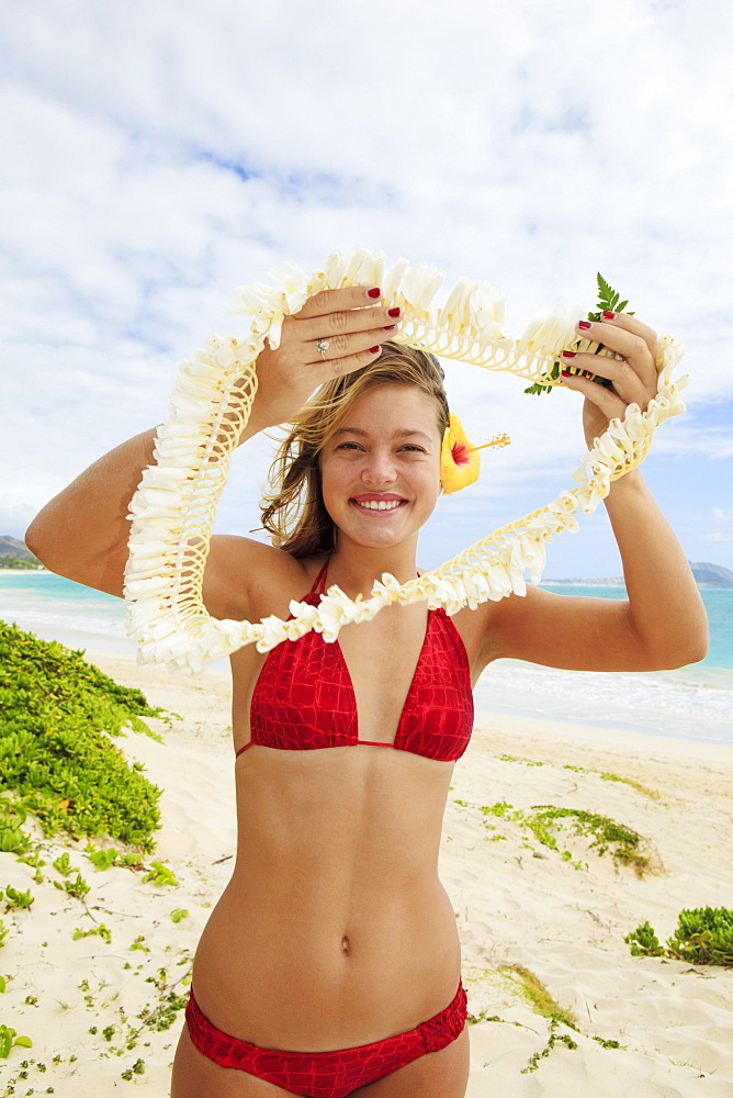 Hawaii, Oahu, Young woman offers lei on beach.