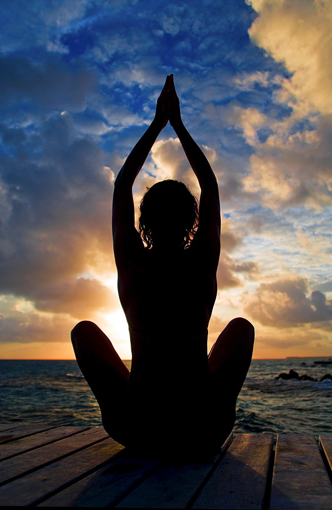 Silhouette of woman doing yoga on oceanside pier.