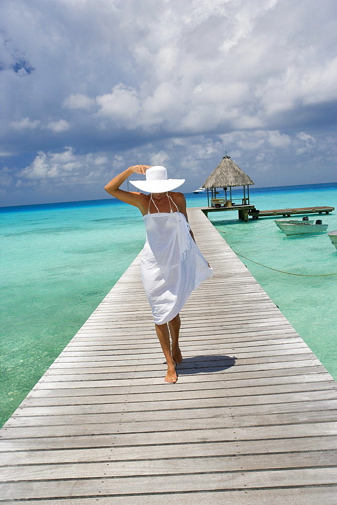 French Polynesia, Tuamotu Islands, Rangiroa Atoll, Woman in white walking on ocean pier.