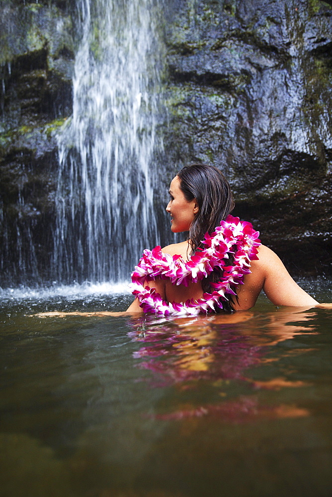 Hawaii, Oahu, Manoa Falls, Beautiful female with orchids leis sitting in a pond at the bottom of Manoa Waterfalls.