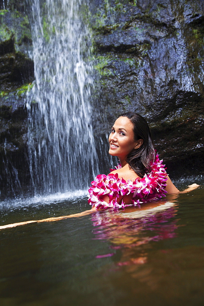 Hawaii, Oahu, Manoa Falls, Beautiful female with orchids leis sitting in a pond at the bottom of Manoa Waterfalls.