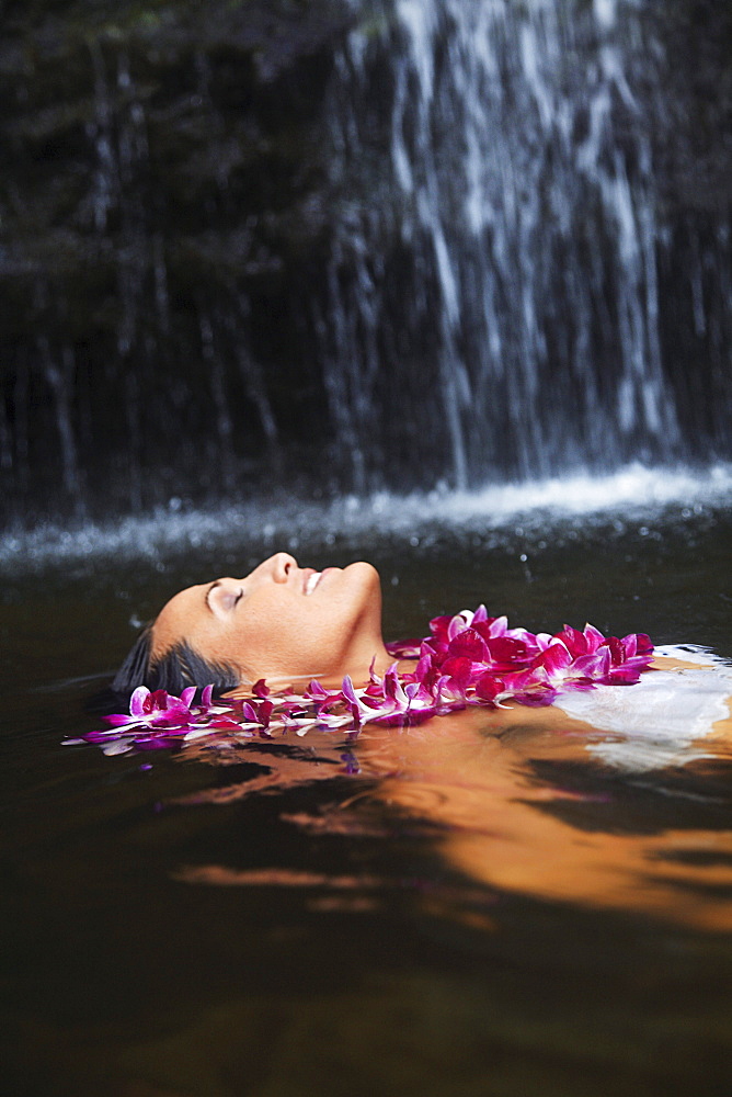 Hawaii, Oahu, Manoa Falls, Beautiful female with orchids leis floating at the bottom of Manoa Waterfalls.