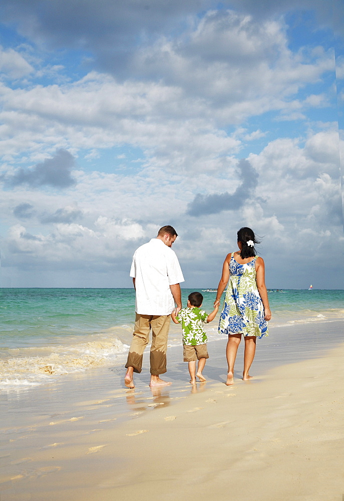 Hawaii, Oahu, Lanikai, Young Family strolling along the beach, view from behind.