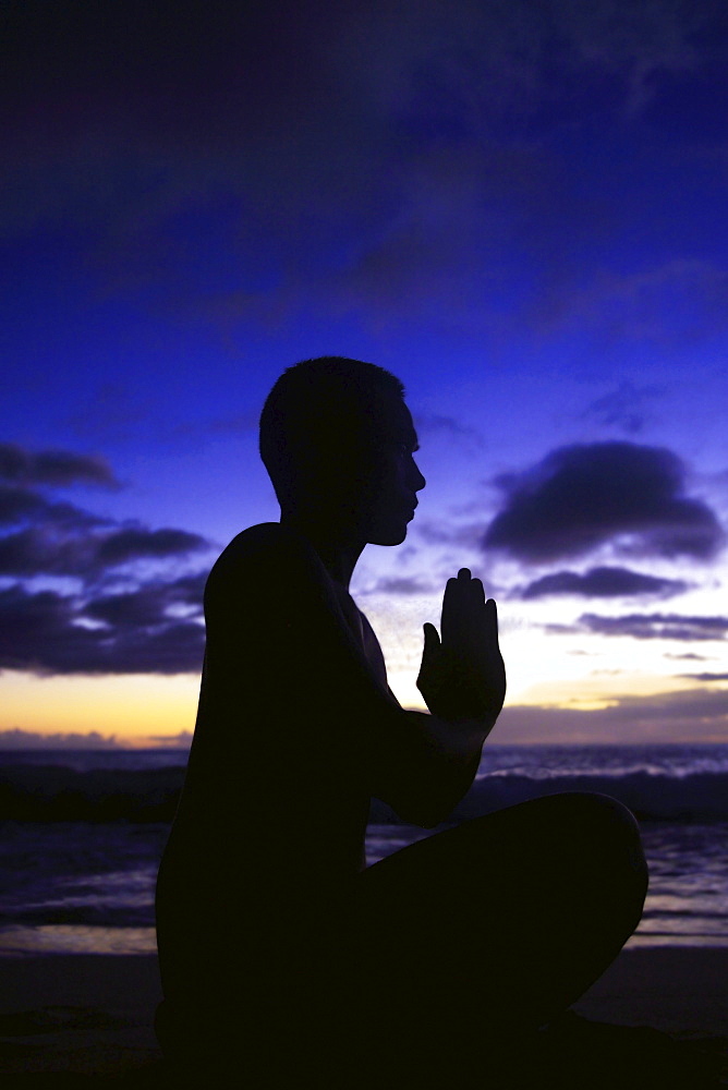 Hawaii, Oahu, Fit young guy on the beach doing yoga on the coastline.