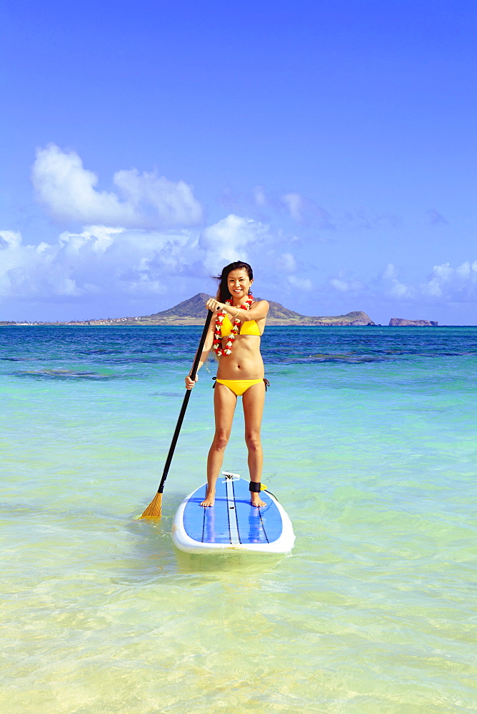 Hawaii, Oahu, Lanikai, Asian women paddle boarding off the beach near Mokulua Island.