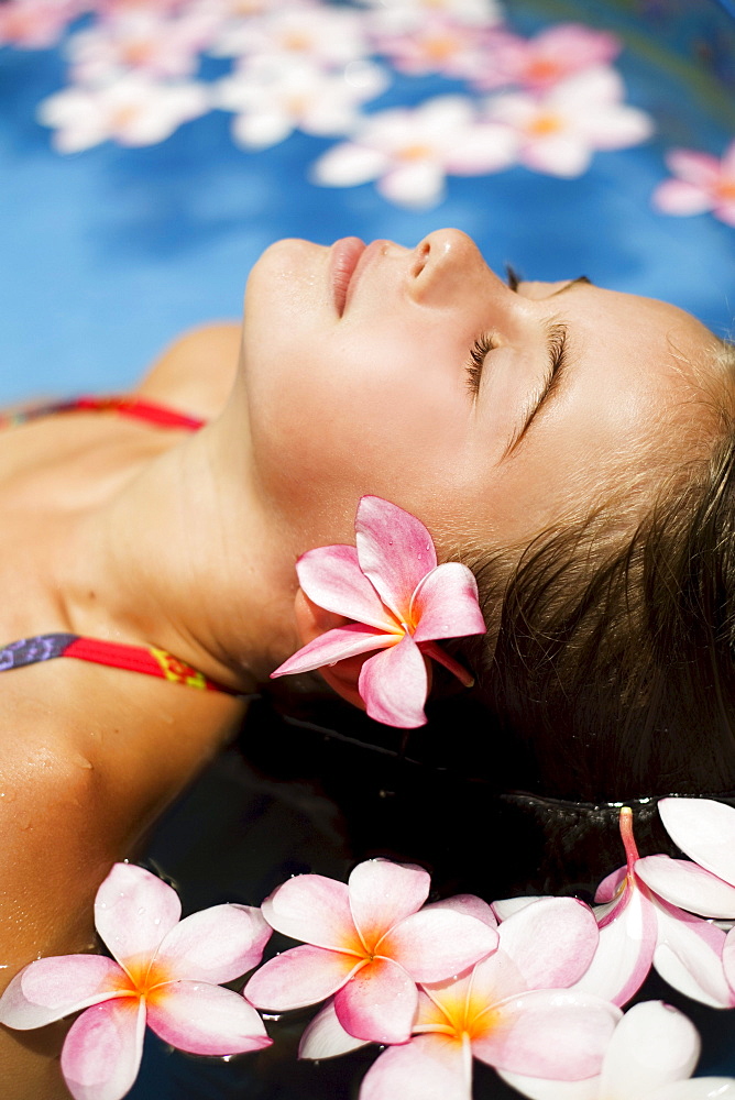 Hawaii, Oahu, Young girl resting in a pool with plumerias.