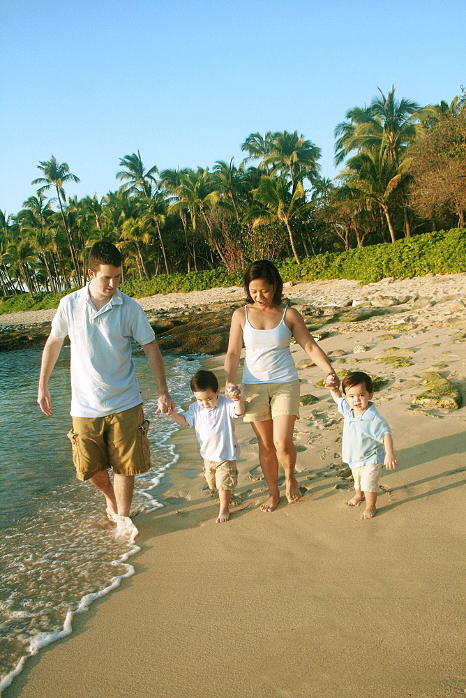 Hawaii, Oahu, North Shore, Young Family holding hands strolling along the beach.